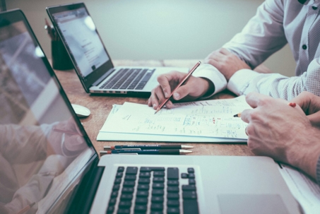signing papers on a desk with two laptops
